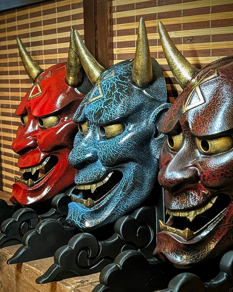 Tres máscaras Hannya en rojo, azul y negro rojizo, con la Marca del Sacrificio en la frente