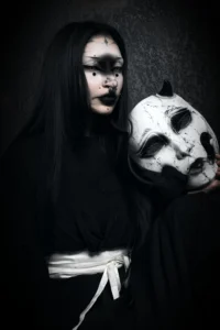 Masque Kuchisake-onna blanc et noir craquelé tenu par une modèle yokai