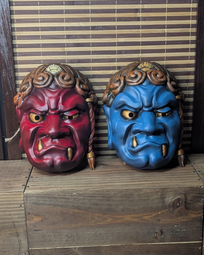 Dos máscaras Fudō Myō-ō, una roja y otra azul, con mirada y colmillos asimétricos