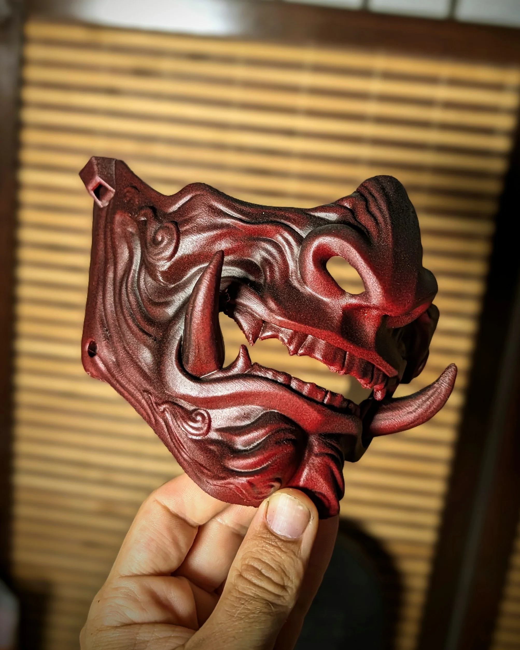 Demi-masque Mempo Oni rouge à dents unies, tenu en main