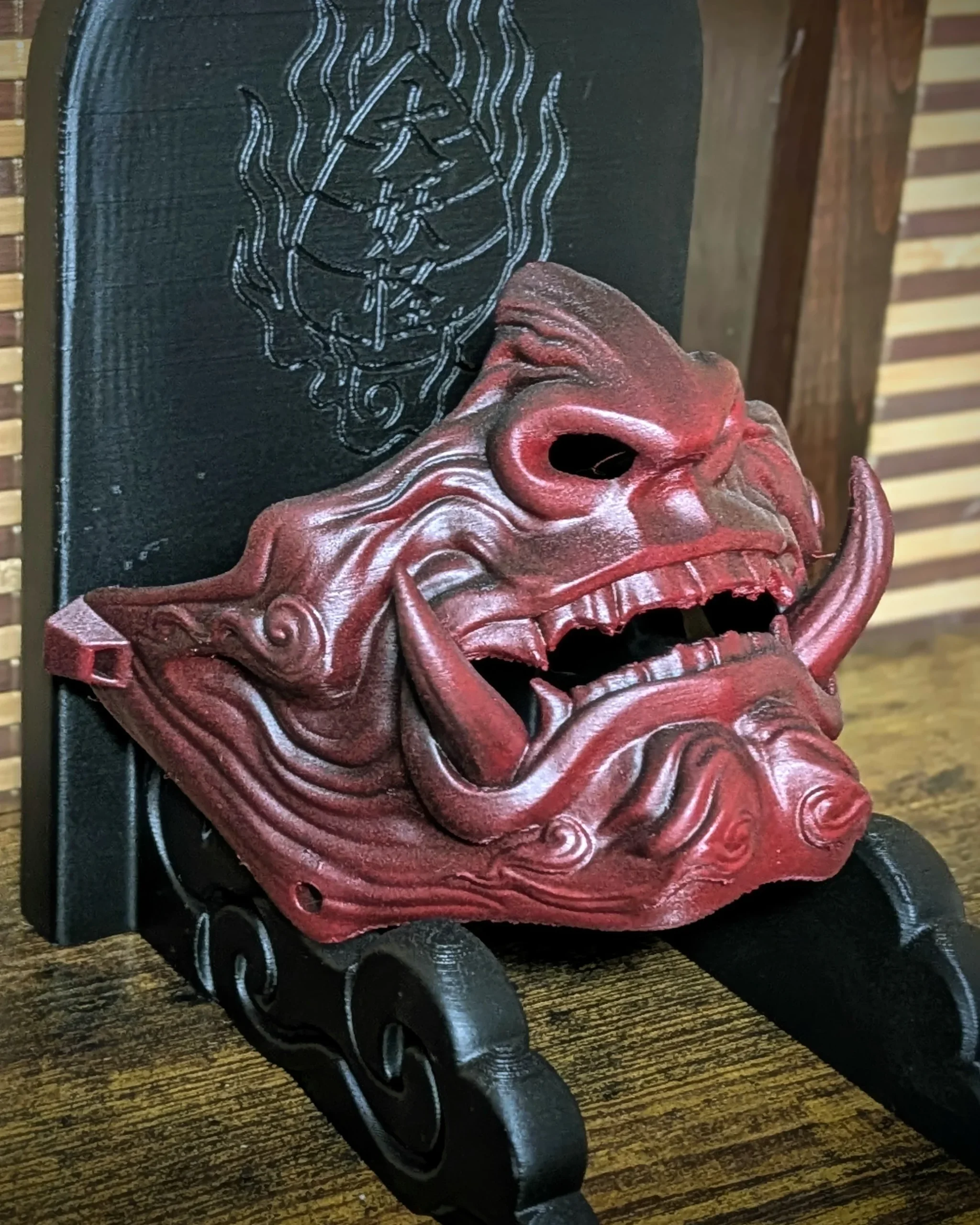 Demi-masque Mempo Oni rouge à dents unies sur un socle de présentation