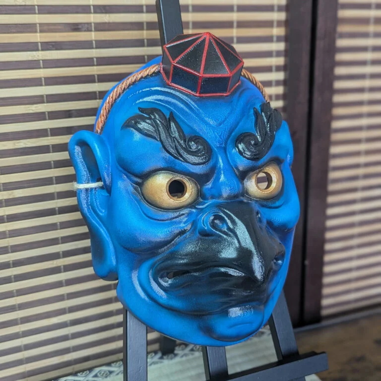 Blue Karasu Tengu warrior mask on a display stand, front-left view