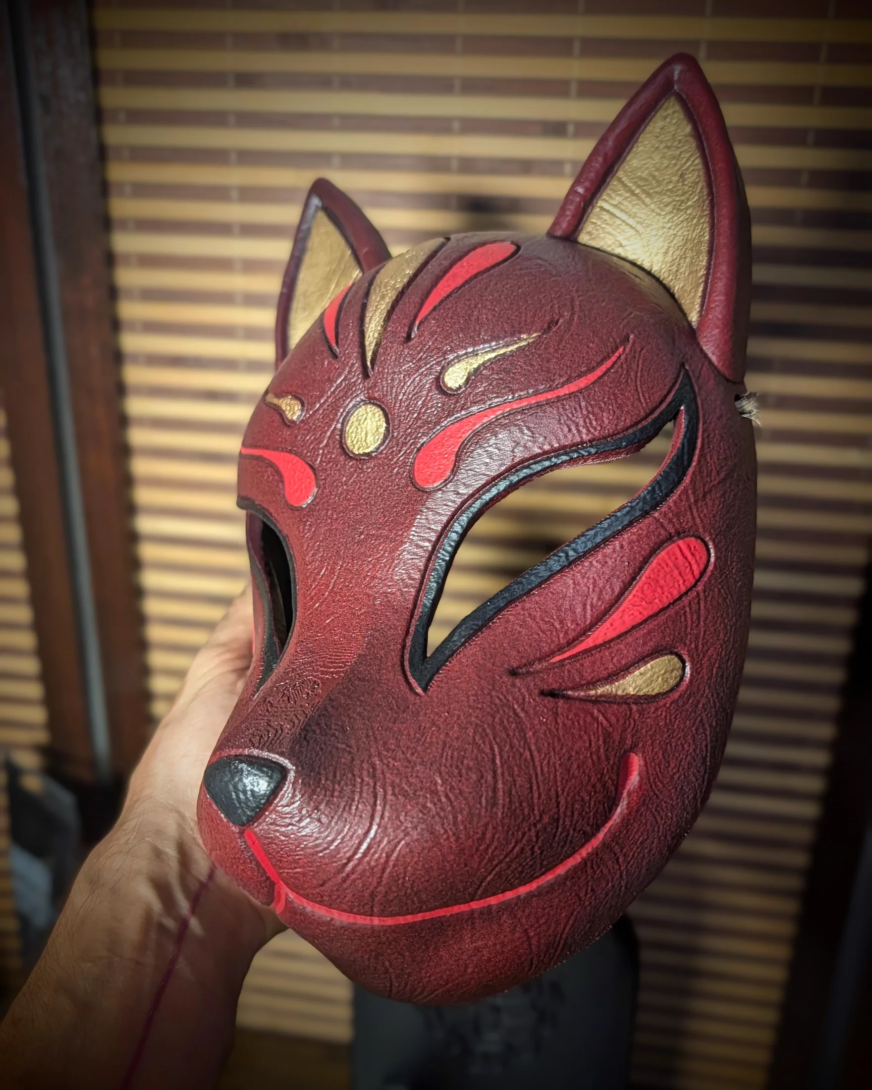 Máscara Kitsune roja vista de perfil, sostenida en la mano