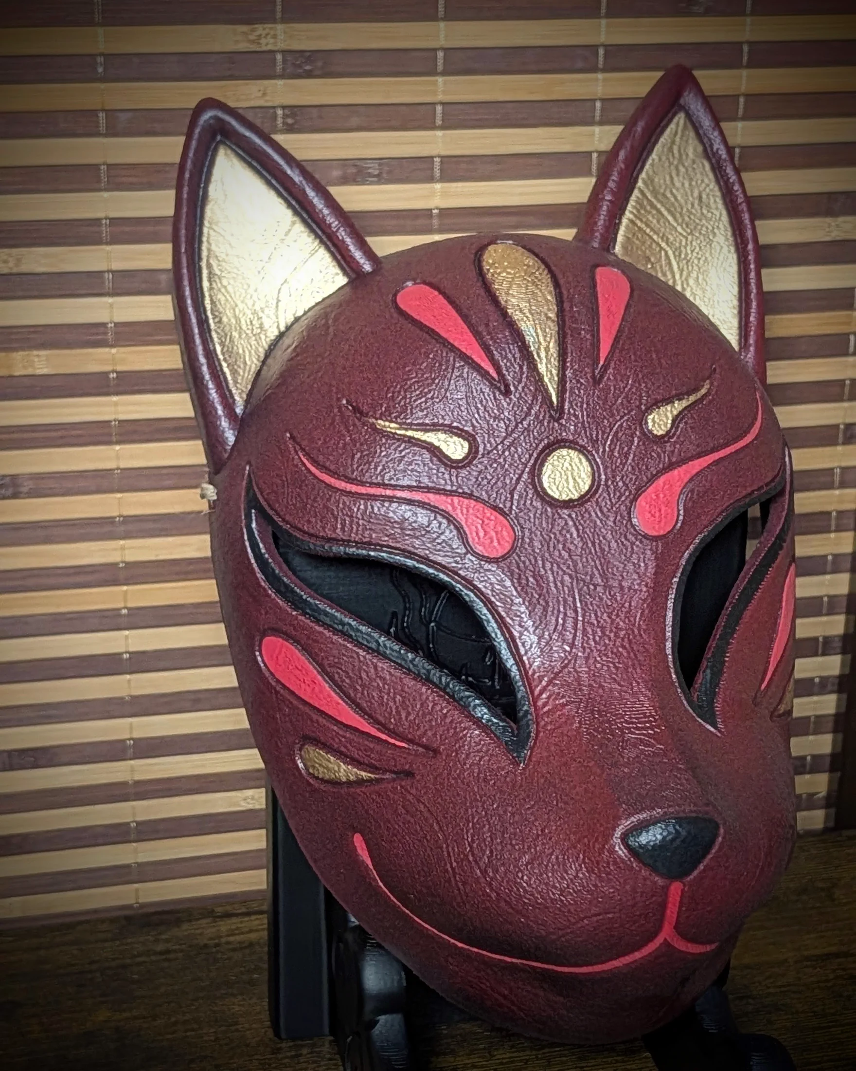 Máscara Kitsune roja vista de tres cuartos sobre su soporte