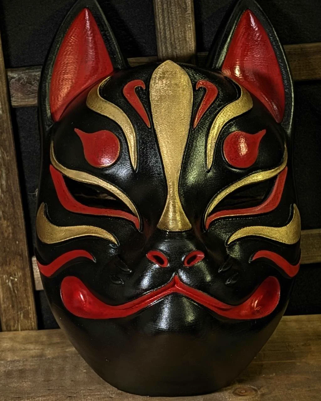 Modern Kitsune mask in black, red and gold on a table, close-up front view
