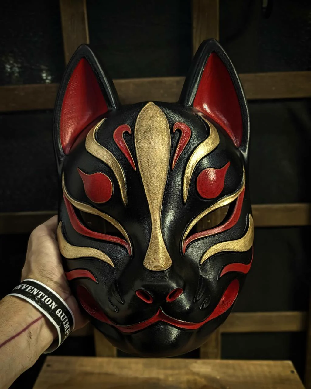 Modern Kitsune mask in black, red and gold, front view held in hand