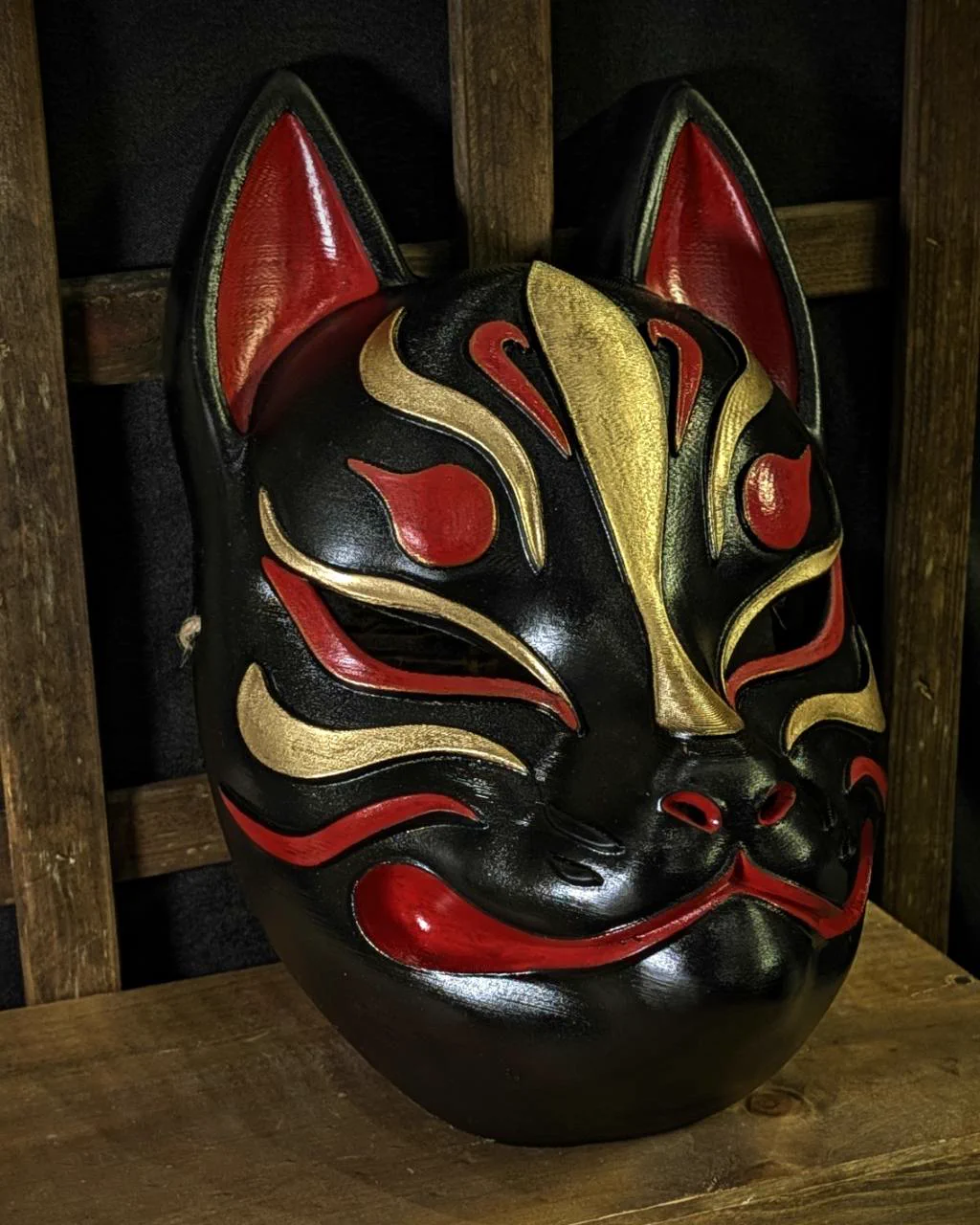 Modern Kitsune mask in black, red and gold on a table, side view