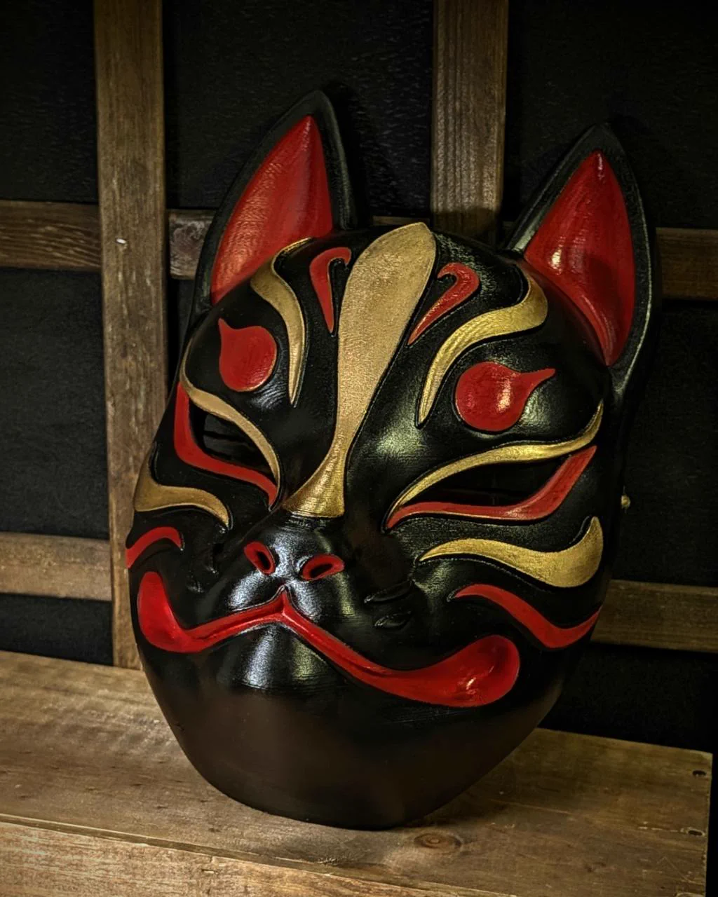 Modern Kitsune mask in black, red and gold on a table, three-quarter view