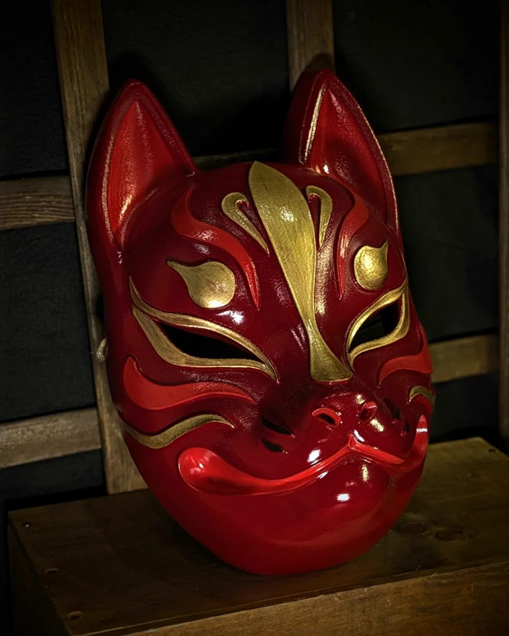 Modern red and gold Kitsune mask on a table, right three-quarter view
