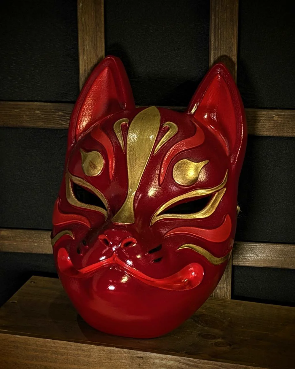 Modern red and gold Kitsune mask on a table, left three-quarter view