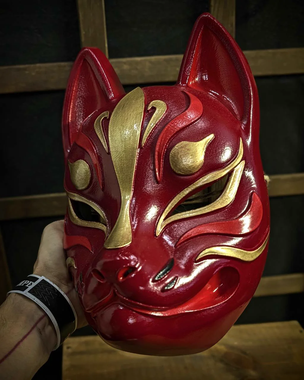 Modern red and gold Kitsune mask held in hand, three-quarter view