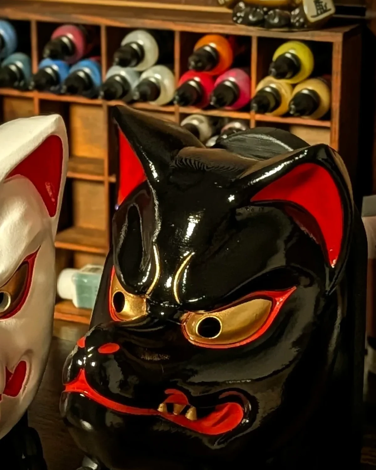 Masque Kitsune noir traditionnel en vue trois quarts, finition noire avec détails rouges et dorés.
