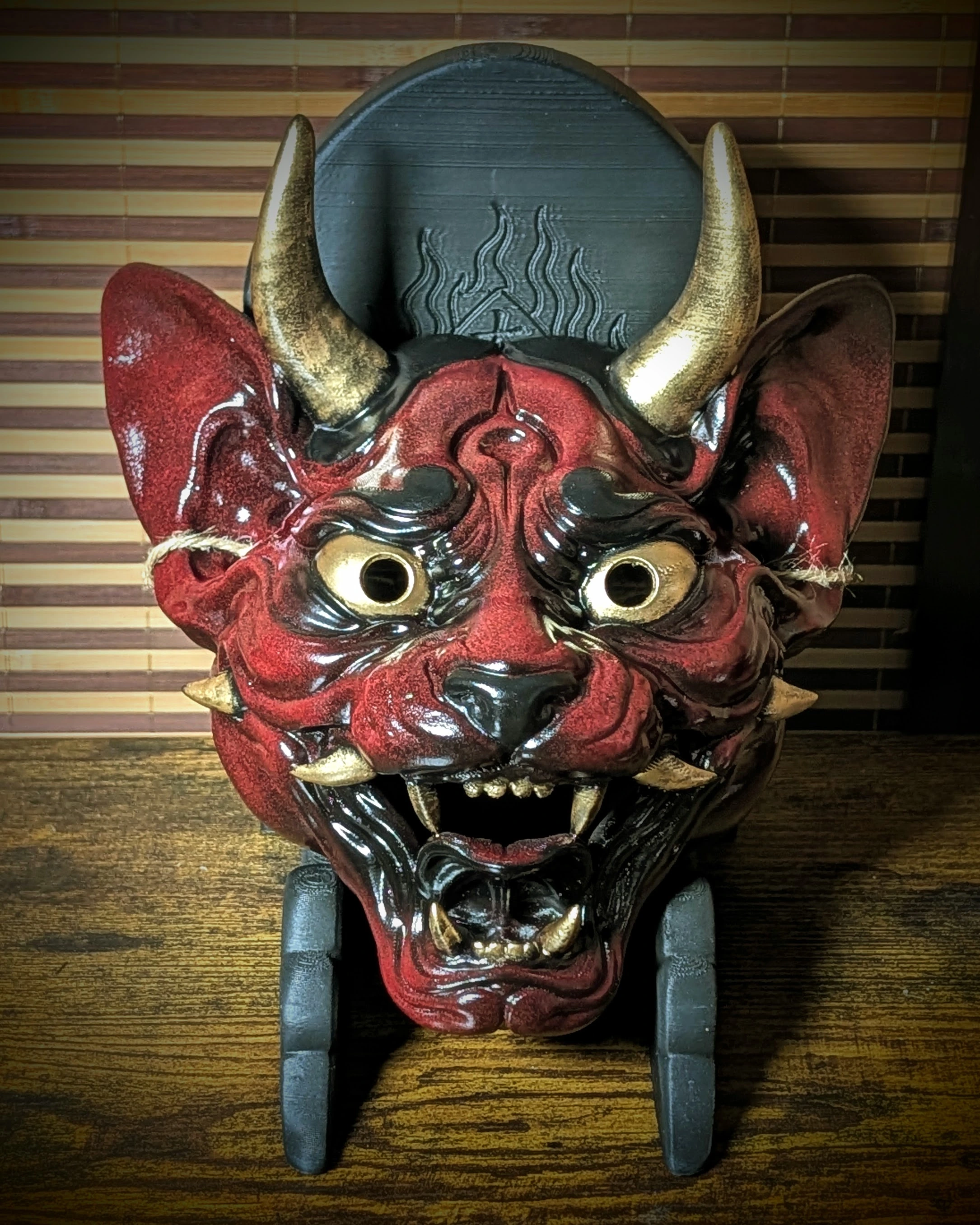 Máscara Neko Hannya completa roja, negra y dorada sobre un soporte