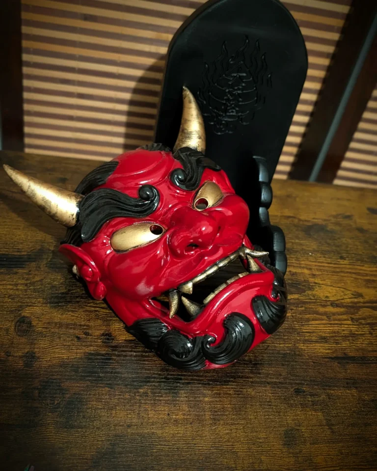 Masque oni gawara rouge posé sur table bois avec socle logo Dai Yokai, vue trois-quarts