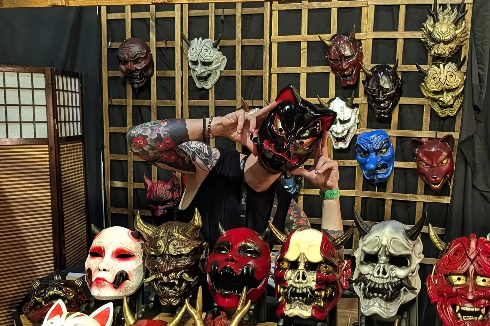 Masque Kitsune noir porté sur le stand Dai Yokai, entouré de masques japonais faits main