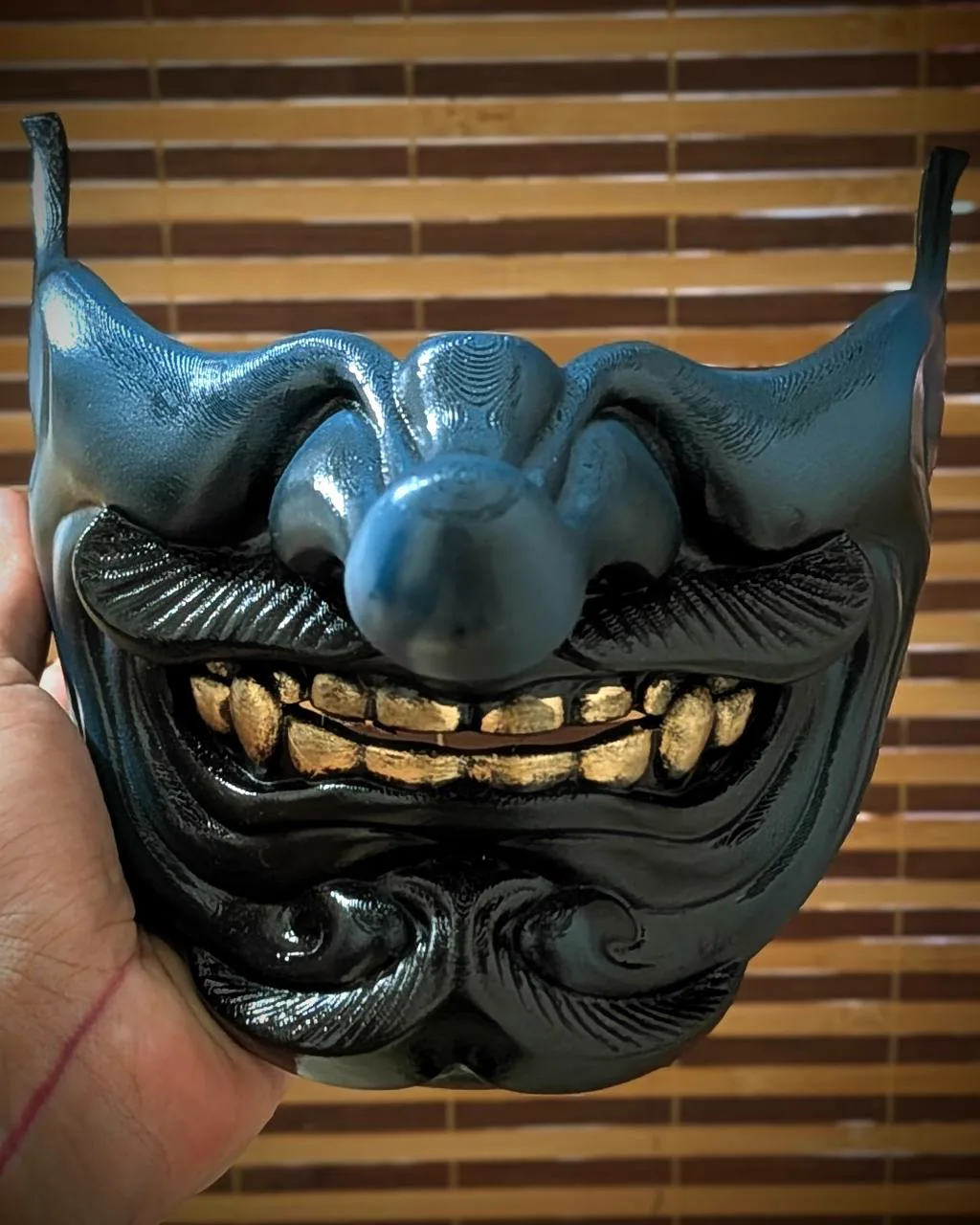 Demi-masque Tengu Kaze bleu et noir avec dents dorées, tenu en main