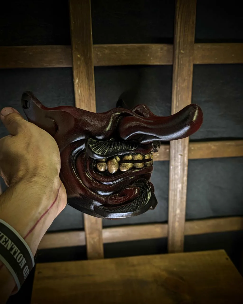 Demi-masque Tengu Kaze rouge et noir avec dents dorées, tenu en main