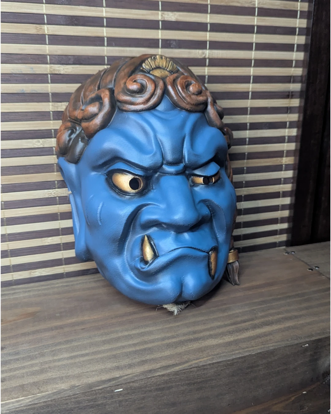 Masque Fudō Myō-ō bleu aux mèches dorées, vue de trois-quarts sur une table