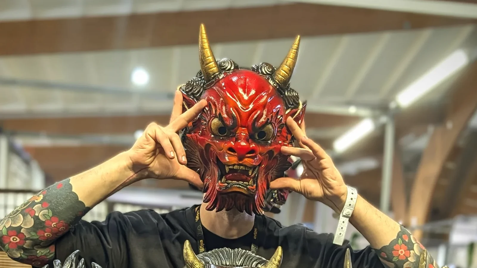Fire red Oni Irezumi mask held in front of a face, with gold horns and hands on either side