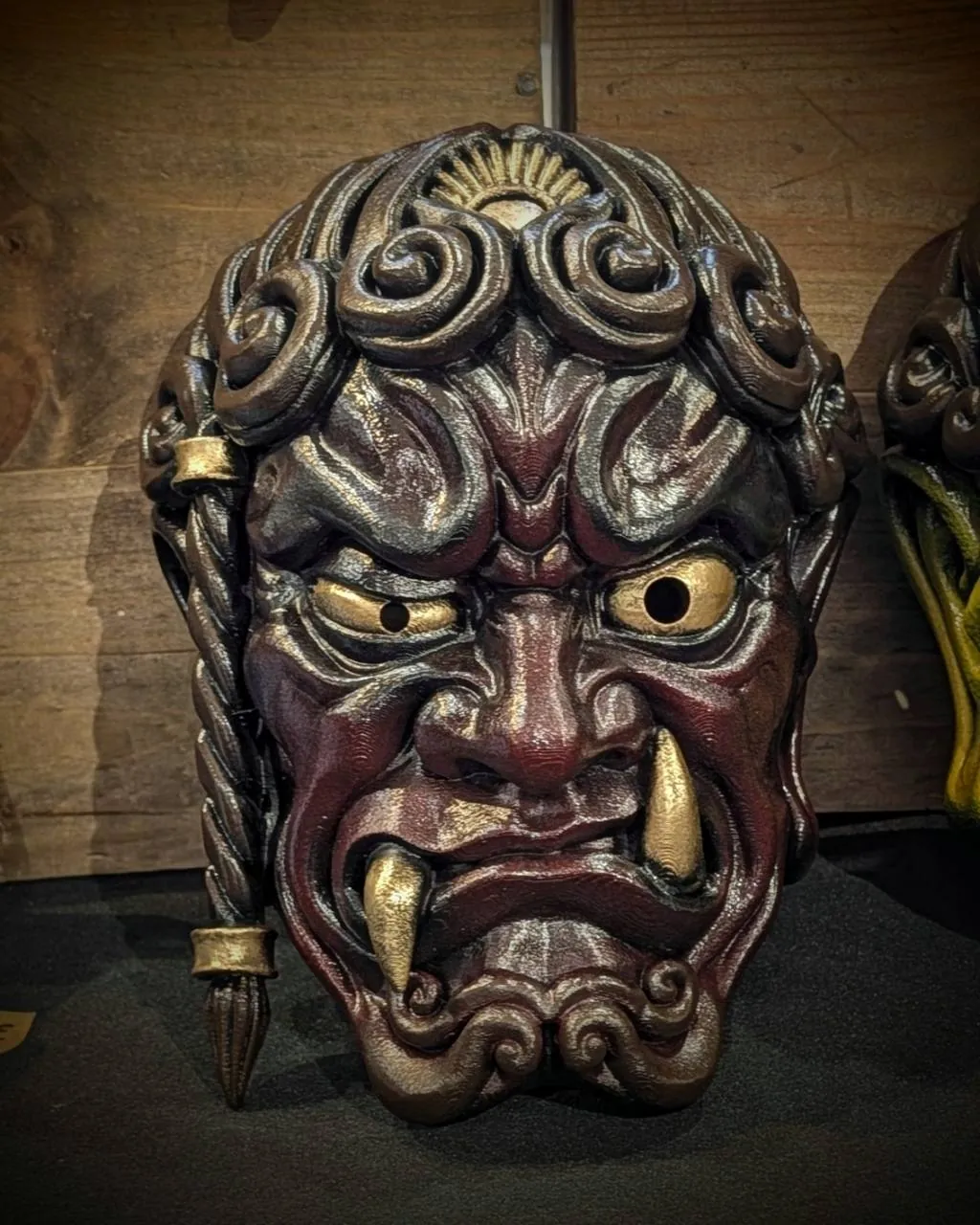 Máscara Fudō Myōō, trenza a la derecha, rojo, vista frontal ante un fondo de madera.